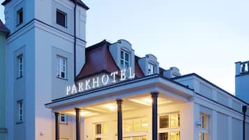 Un hôtel doté d’une entrée imposante, d’une tour et d’une enseigne sur laquelle on peut lire « PARKHOTEL ».