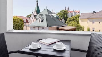 A balcony with wicker chairs, a table, two cups of coffee, and an open book.