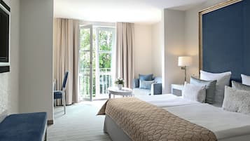 A hotel room with a large bed, a seating area with a table and chairs, and a view through a glass door.