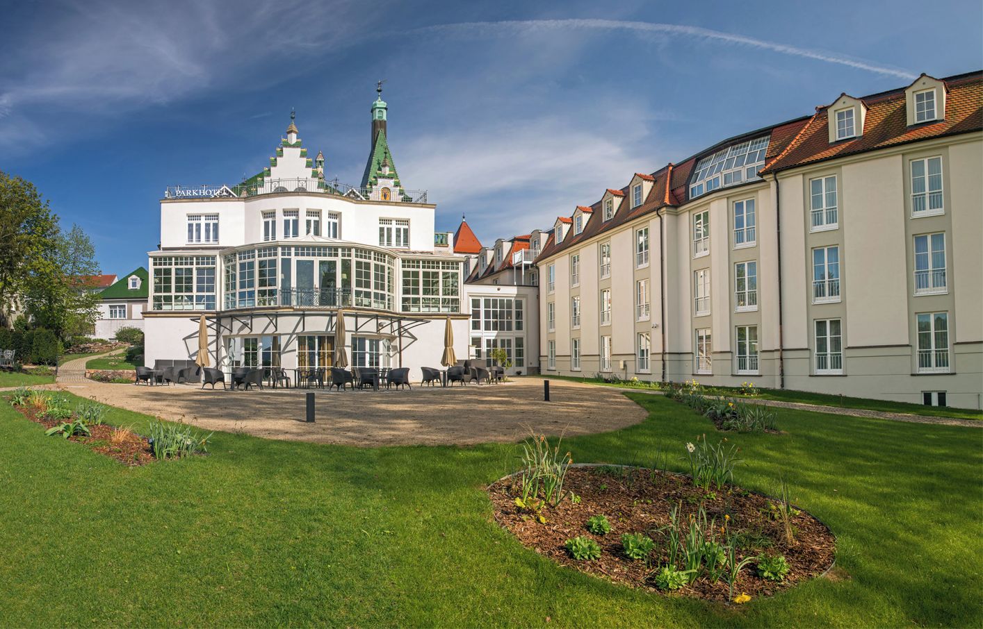 Un grand bâtiment historique doté d’une structure centrale en verre, entouré d’une pelouse bien entretenue et d’une rangée de bâtiments traditionnels.
