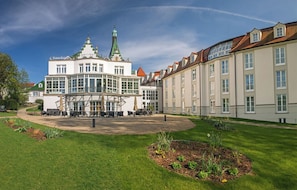 Un grand bâtiment historique doté d’une structure centrale en verre, entouré d’une pelouse bien entretenue et d’une rangée de bâtiments traditionnels.