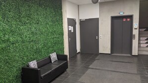 Un hall d’entrée agrémenté d’un mur végétal, d’un canapé en cuir noir avec des coussins à motifs zébrés, et d’un escalier menant à un ascenseur.