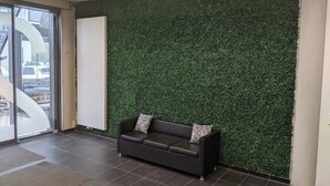 Un espace d’accueil avec un canapé marron foncé, un tableau blanc et un mur recouvert d’un gazon artificiel vert.