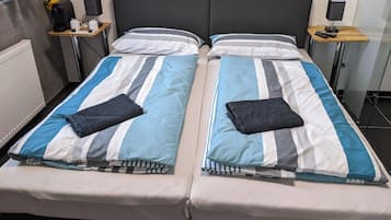 A double bed with striped bedding, two bedside tables with lamps, a radiator, and a small shelf with items.