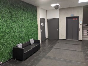 A lobby with a green wall, a black leather sofa with zebra-patterned cushions, and a staircase leading to an elevator. - Business-motel mit Xl-parking (Heimsheim)