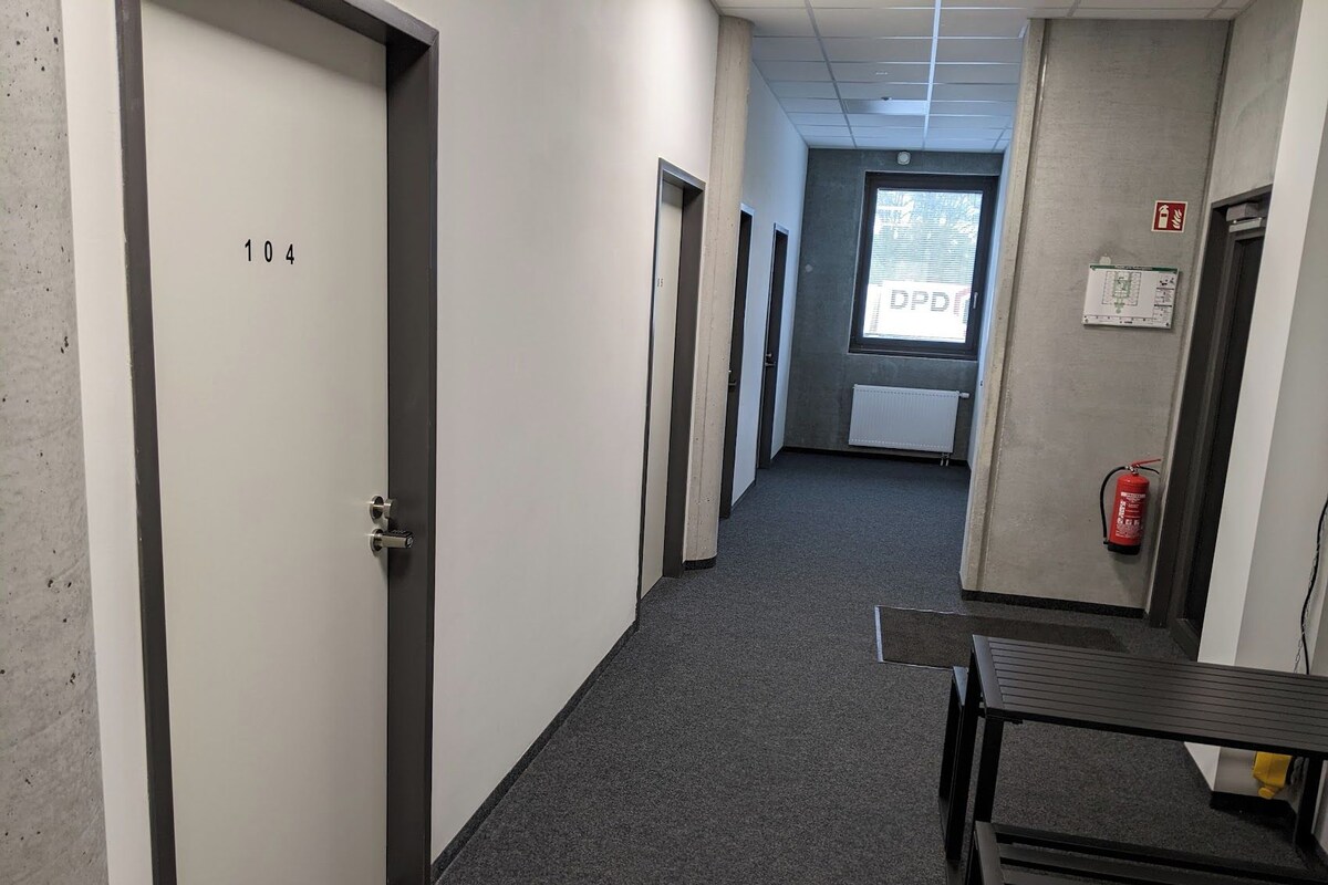 A corridor with doors numbered 104 and 105, a fire extinguisher, and a window with a view of trees.