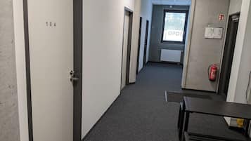 A corridor with doors numbered 104 and 105, a fire extinguisher, and a window with a view of trees.