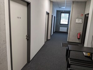 Pasillo con puertas numeradas 104 y 105, un extintor y una ventana que da a árboles.