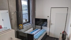 A compact hotel room with a single bed, a bedside TV, a small bathroom with a sink and mirror, and a window with blinds. - Business-motel mit Xl-parking (Heimsheim)