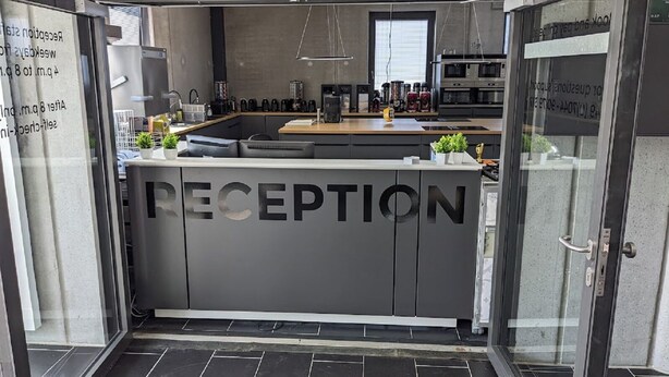 Un espace d’accueil avec un comptoir de réception gris, une machine à café et un four à micro-ondes.