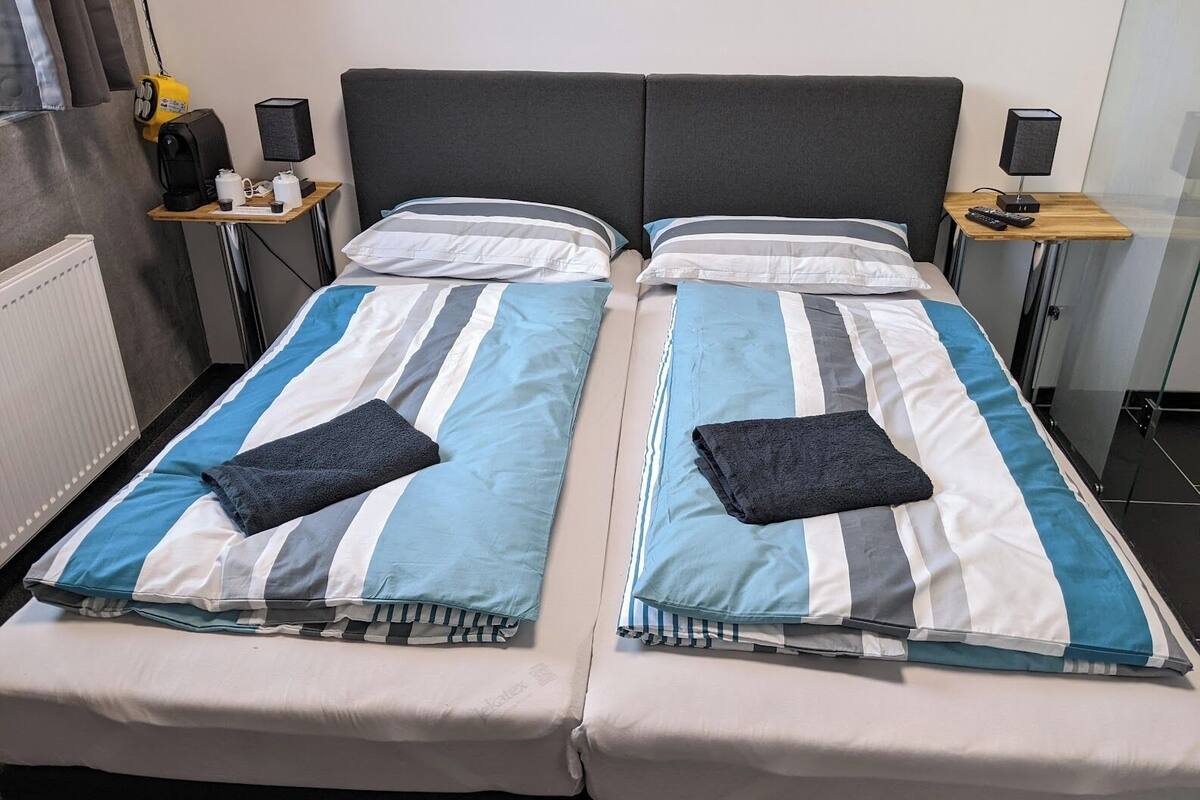 Una cama doble con ropa de cama a rayas, dos mesitas de noche con lámparas y un radiador.