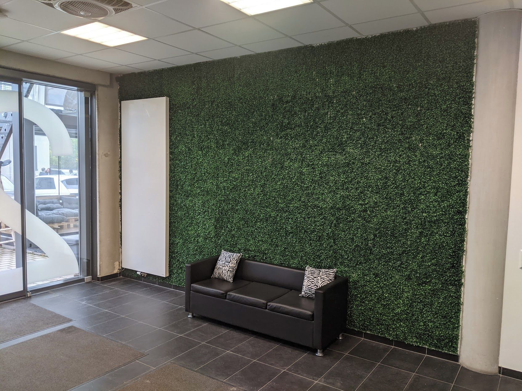 A reception area with a dark brown sofa, a whiteboard, and a green artificial grass wall.