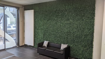 A reception area with a dark brown sofa, a whiteboard, and a green artificial grass wall.