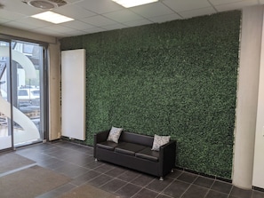 Zona de recepció amb un sofà marró fosc, una pissarra i una paret de gespa artificial verda.
