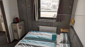 A small, compact room with a bed, a radiator, a small table, and a window with blinds. - Business-motel mit Xl-parking (Heimsheim)