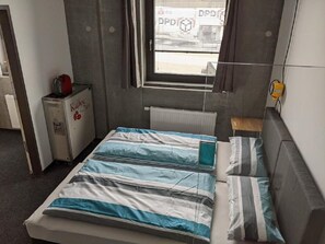 A small, compact room with a bed, a radiator, a small table, and a window with blinds. - Business-motel mit Xl-parking (Heimsheim)