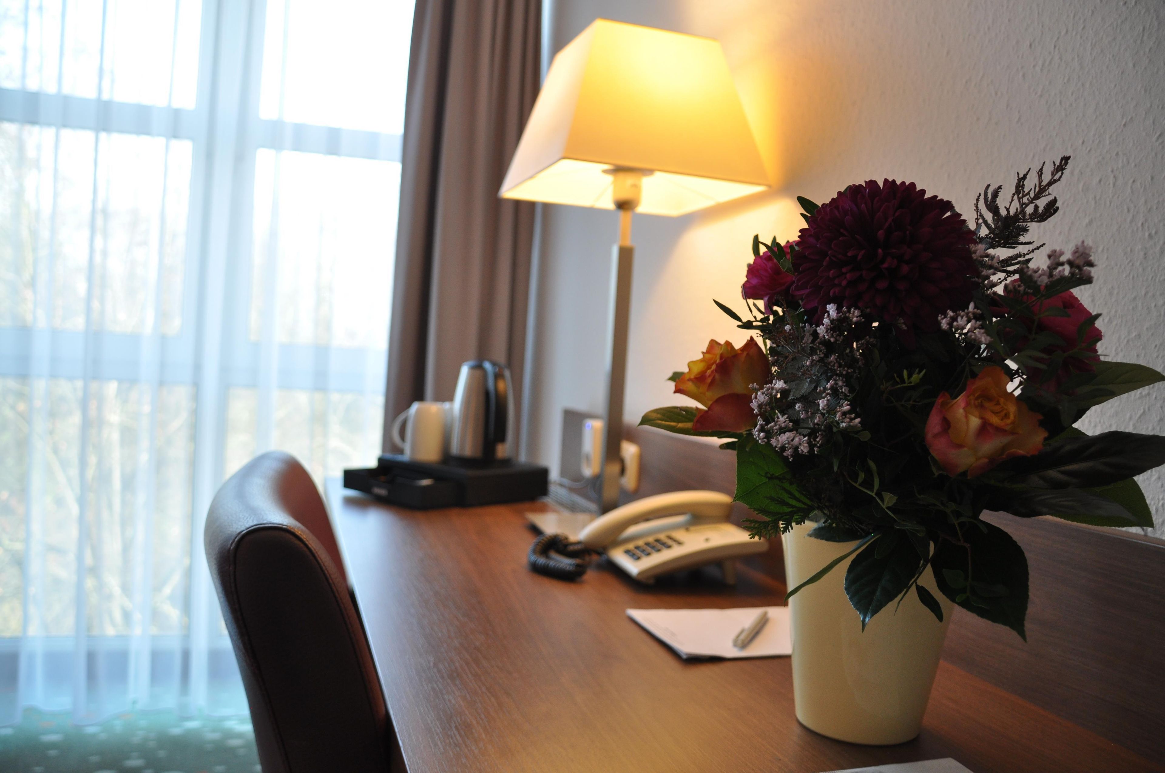 Ein Hotelzimmer mit einem Holztisch, einer Lampe, einem Telefon und einer Blumenvase.