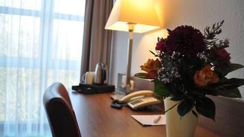 Ein Hotelzimmer mit einem Holztisch, einer Lampe, einem Telefon und einer Blumenvase.