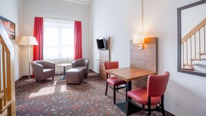 A hotel room with a wooden table, red chairs, a TV mounted on the wall, and a window with red curtains. - Best Western Hotel Erlangen (Erlangen)