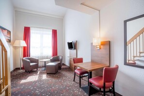 A hotel room with a wooden table, red chairs, a TV mounted on the wall, and a window with red curtains. - Best Western Hotel Erlangen (Erlangen)