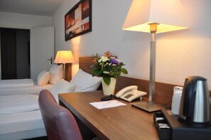 Une chambre d’hôtel comprenant un lit, un bureau avec une lampe, un téléphone, une machine à café et un vase avec des fleurs.