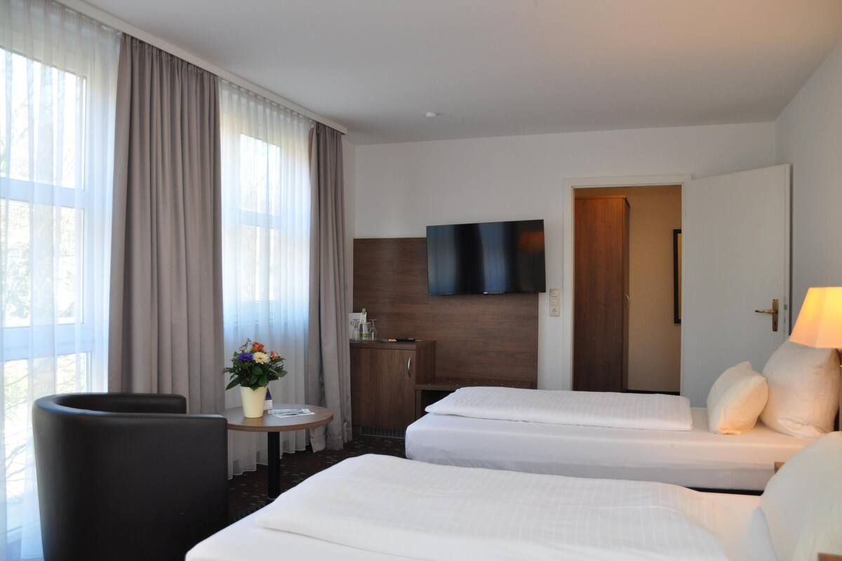 A hotel room with two beds, a TV mounted on the wall, a small table with a vase of flowers, and a chair.