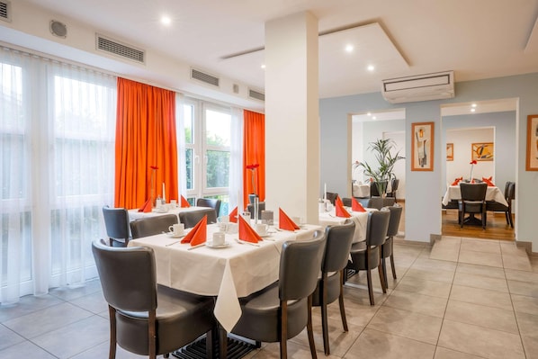 A dining area with tables set for service, a large window with orange curtains, and a view of the outdoors. - Best Western Hotel Erlangen (Erlangen)