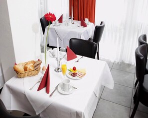 A dining table set with breakfast items, including bread, eggs, and fruit, in a room with white walls and red curtains. - Best Western Hotel Erlangen (Erlangen)