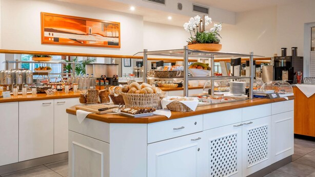 A modern kitchen with white cabinets, stainless steel appliances, and a variety of food items displayed on the counter. - Best Western Hotel Erlangen (Erlangen)