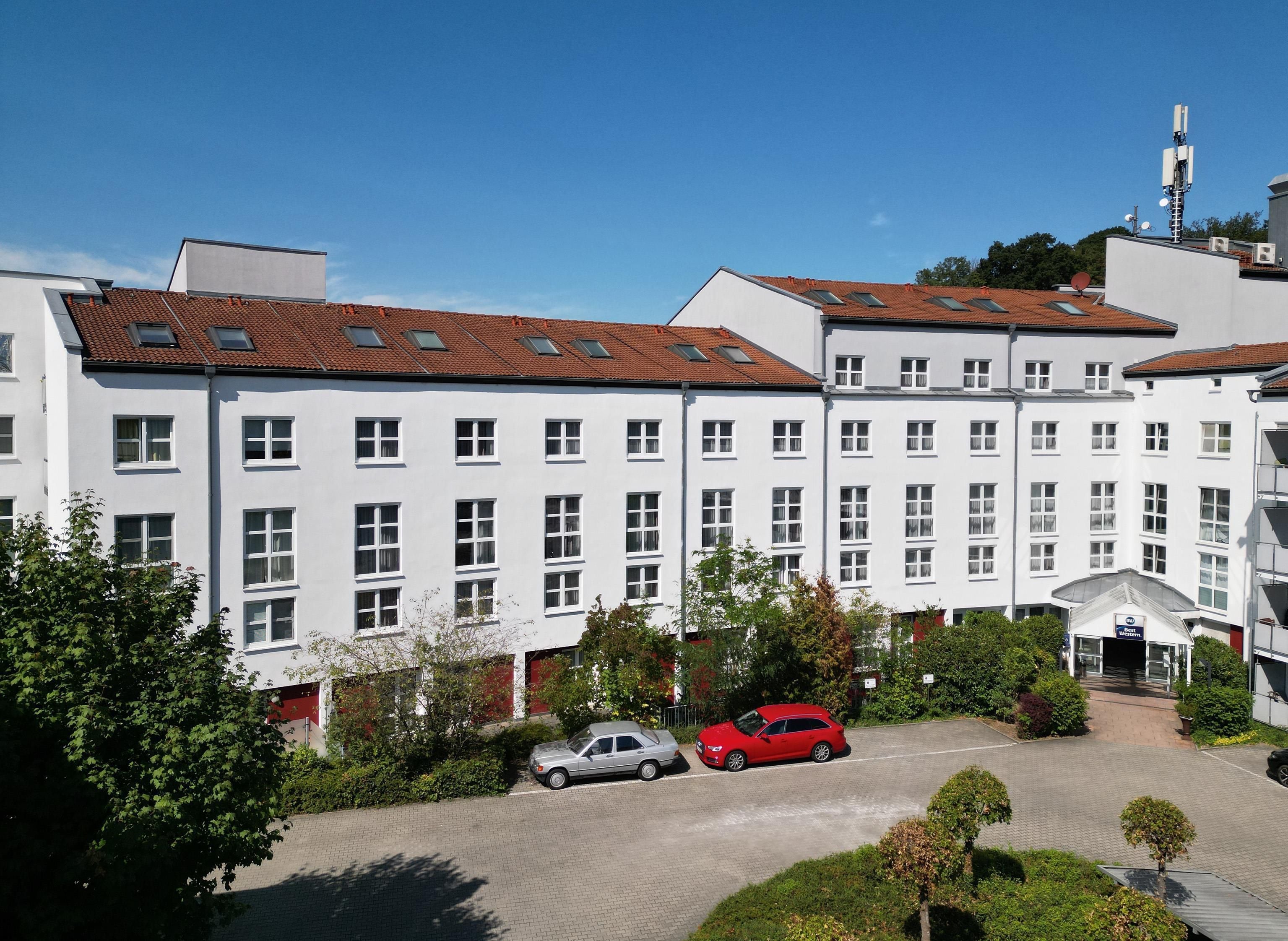 Ein mehrstöckiges Gebäude mit einer Reihe von Fenstern, einem Parkplatz mit Autos und blauem Himmel.