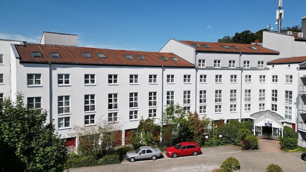 A multi-story building with a row of windows, a parking area with cars, and a clear sky. - Best Western Hotel Erlangen (Erlangen)