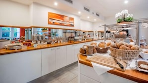 Un moderno bufé de desayuno con una variedad de alimentos, incluyendo pan y bollería, y un amplio ventanal que proporciona luz natural.