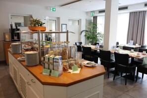 A hotel breakfast area with a buffet counter, dining tables, chairs, and potted plants. - Best Western Hotel Erlangen (Erlangen)