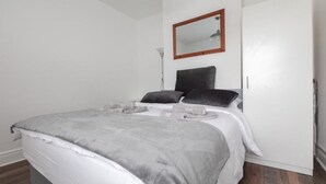 Une chambre à coucher avec un lit, des oreillers, une table de chevet, un miroir et une porte.