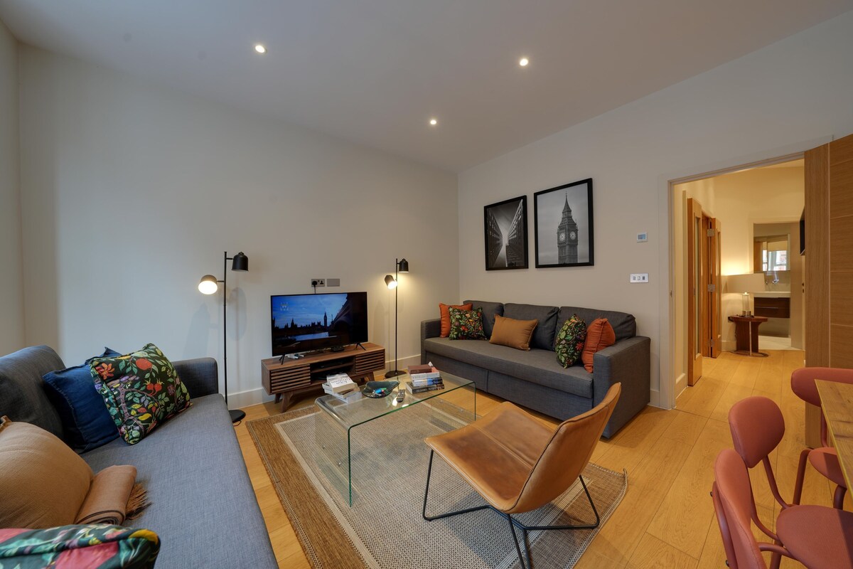 Ein modernes Wohnzimmer mit einer Couch, Sesseln, einem Glastisch, einem Fernseher und einem Kamin.