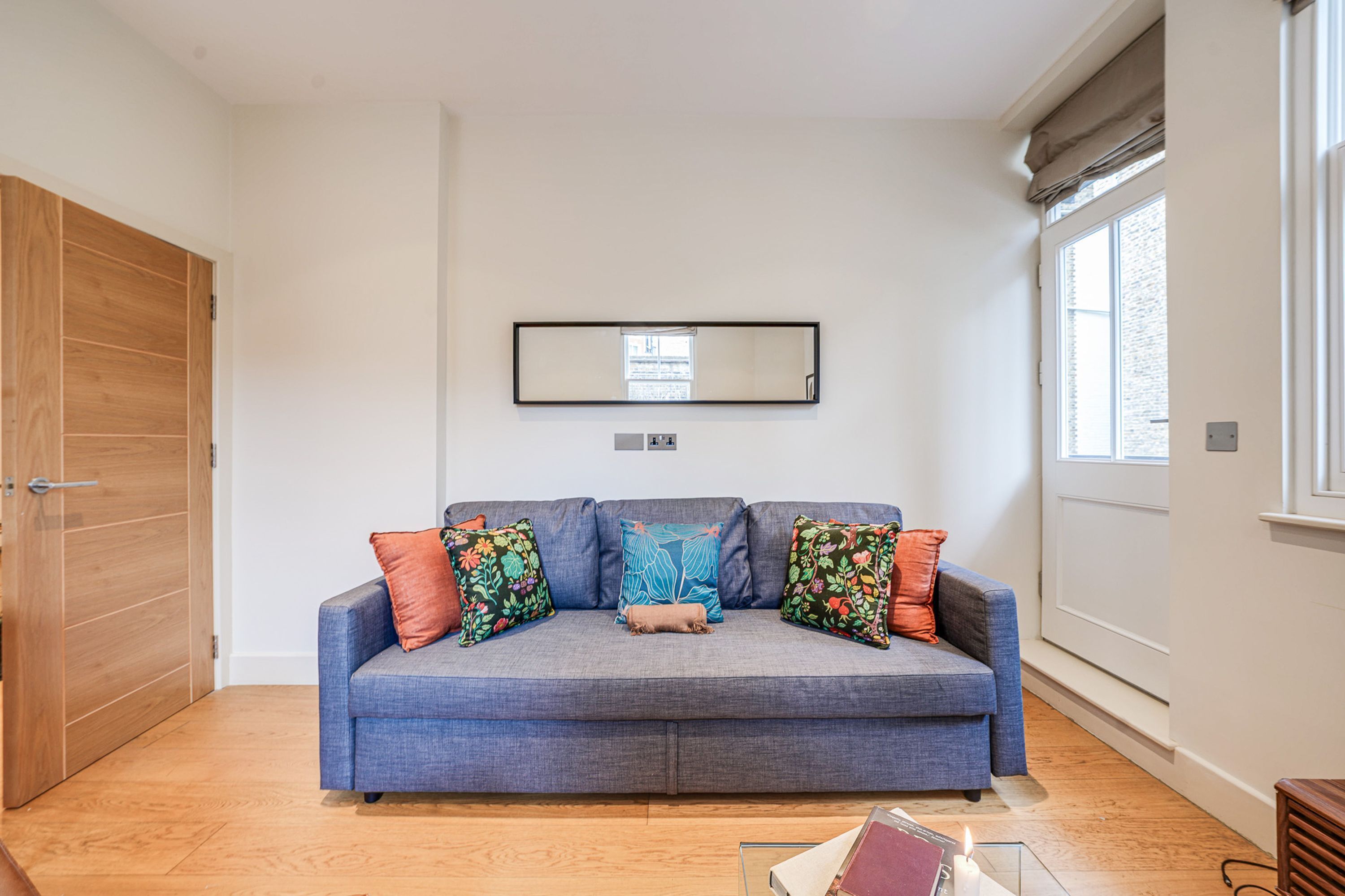 A room with a sofa, a mirror, a window, and a door.