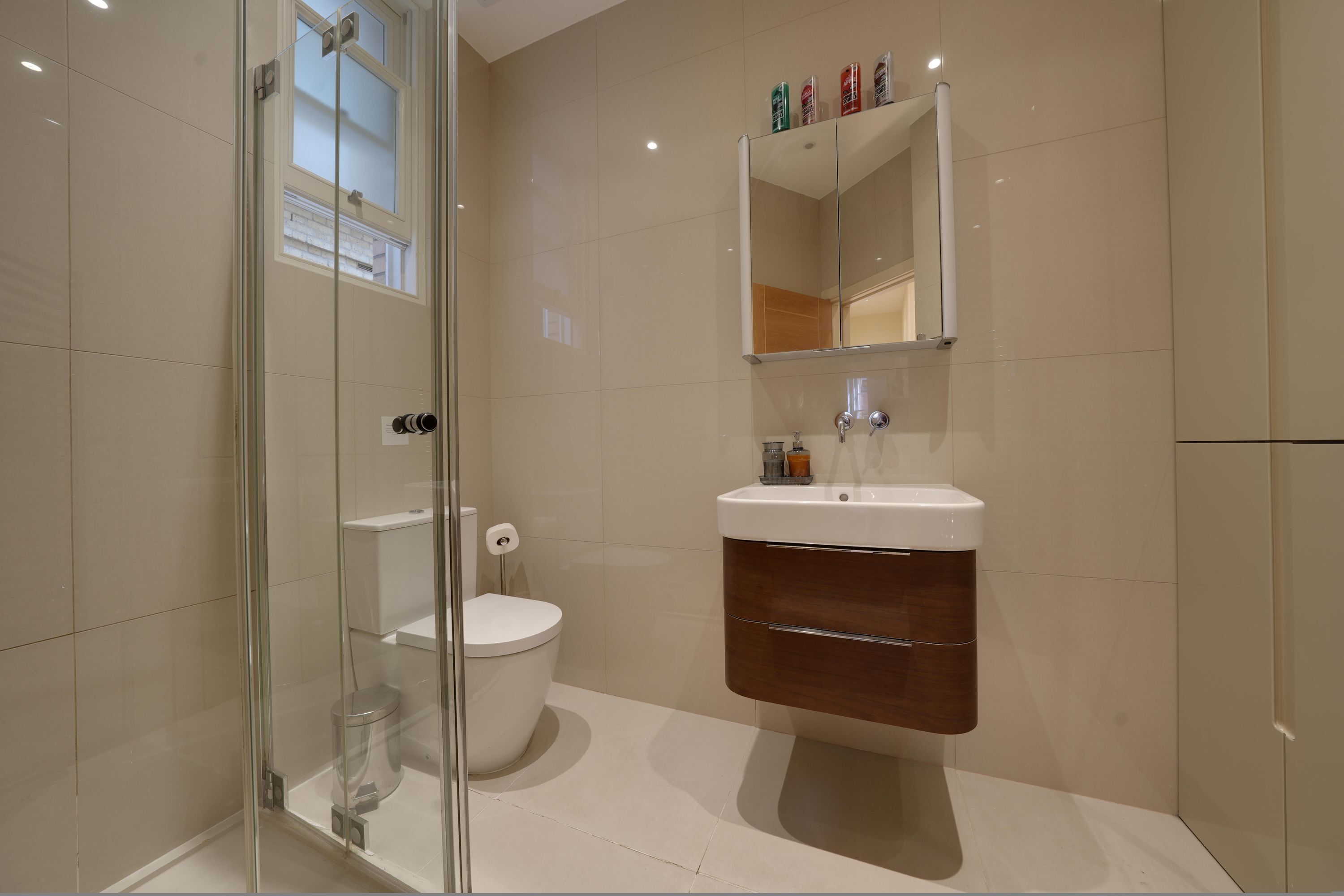 Une salle de bain moderne avec une douche à parois de verre, des toilettes blanches et un meuble-lavabo en bois avec un miroir au-dessus.