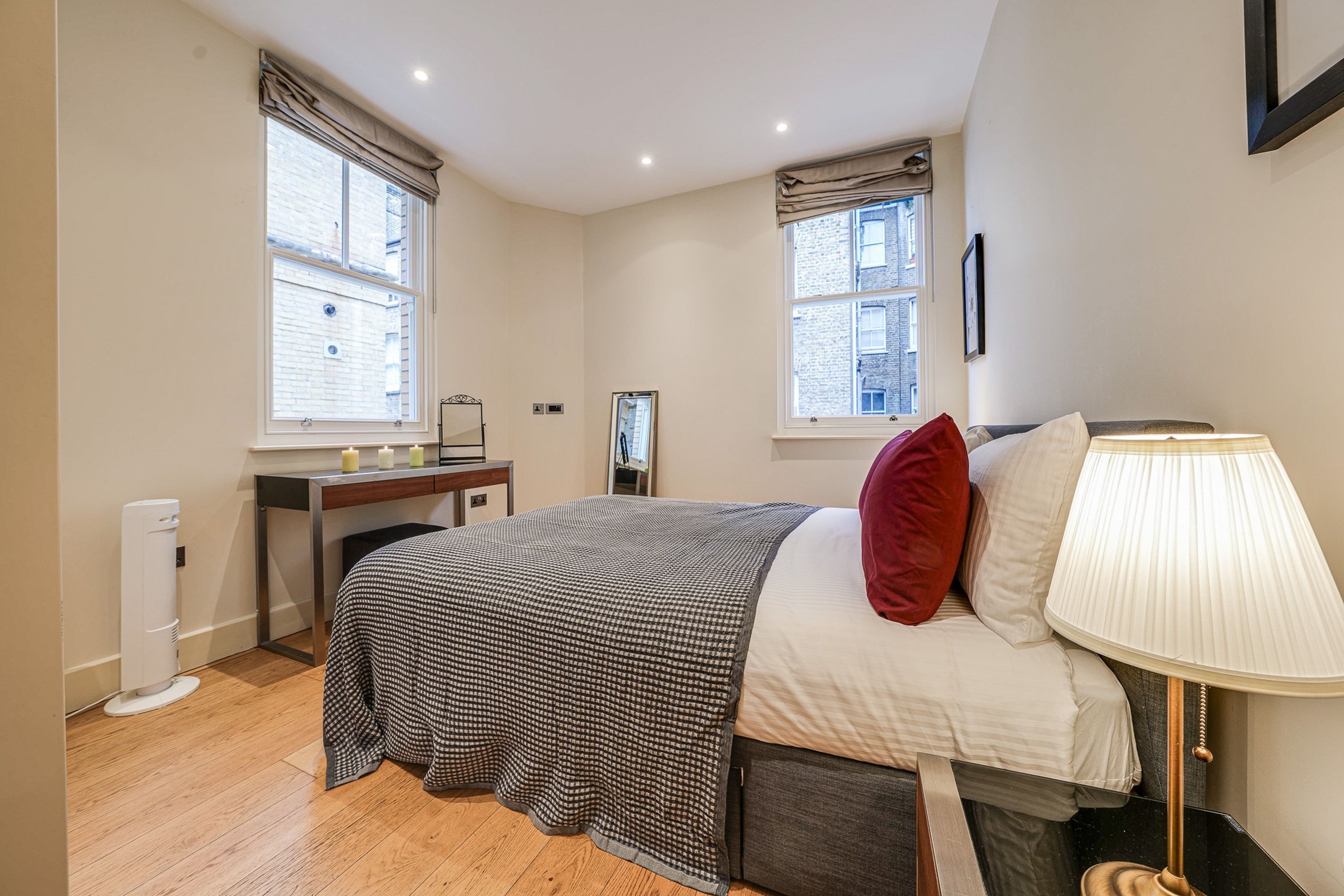 A bedroom with a bed, bedside table, lamp, and two windows.