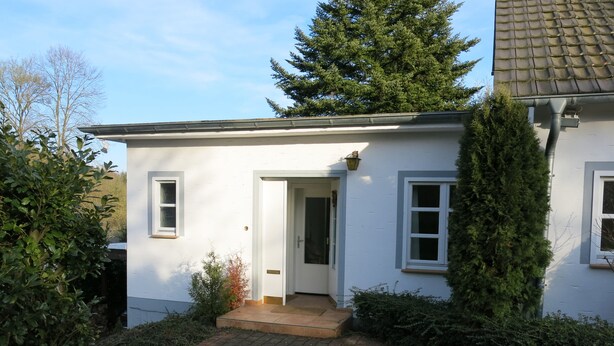 Une maison blanche avec un toit en tuiles, une porte d’entrée et un petit porche.