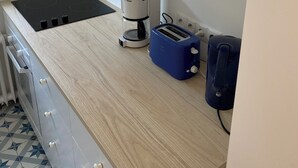 Une cuisine avec une plaque de cuisson noire, une machine à café, un grille-pain bleu et une valise posée sur le comptoir.