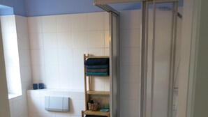 Une salle de bain comprenant des toilettes, une douche avec une porte en verre et une étagère avec des serviettes et des articles de toilette.