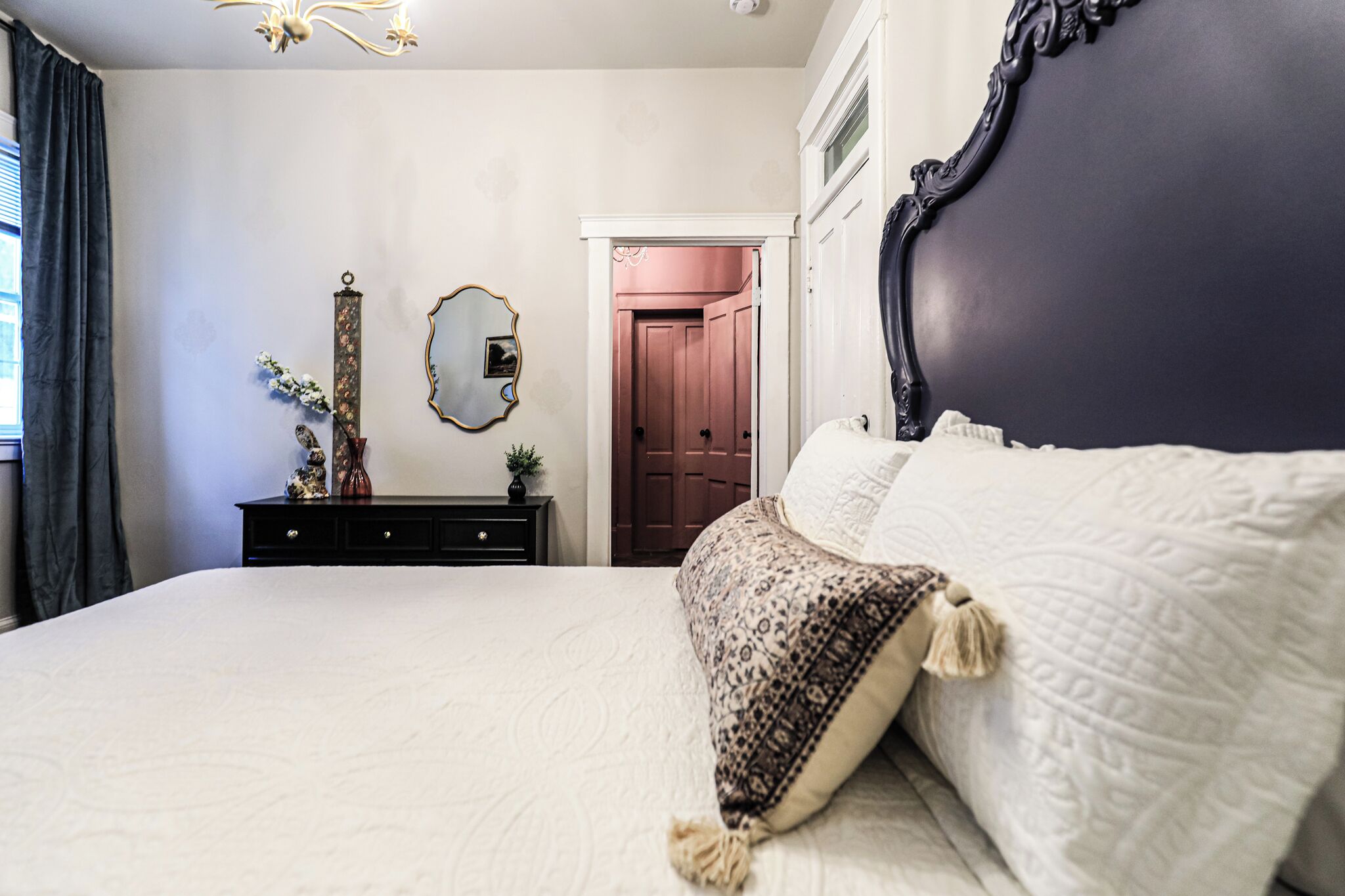 Un dormitorio con una cama grande, un aparador, un espejo y una puerta que da a otra habitación.