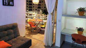 Un salon comprenant un canapé, une table à manger avec des chaises, un lustre et une vue sur un balcon doté d’une balustrade.