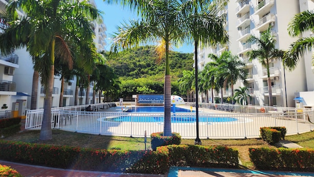 Un quartier résidentiel doté d’une piscine entourée de palmiers, avec des collines en arrière-plan.