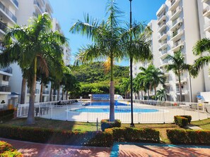 A residential area with a swimming pool surrounded by palm trees and a hilly backdrop. - Beautiful apartment surrounded by nature (Girardot)