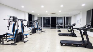 Une salle de sport équipée de divers appareils d’exercice, notamment des tapis de course et des appareils de musculation, et dotée de grandes fenêtres offrant une vue sur l’extérieur.