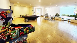 Un grand espace intérieur comprenant une table de billard, une table de billard sur le thème de Mario et une borne d’arcade sur le thème de Super Mario.