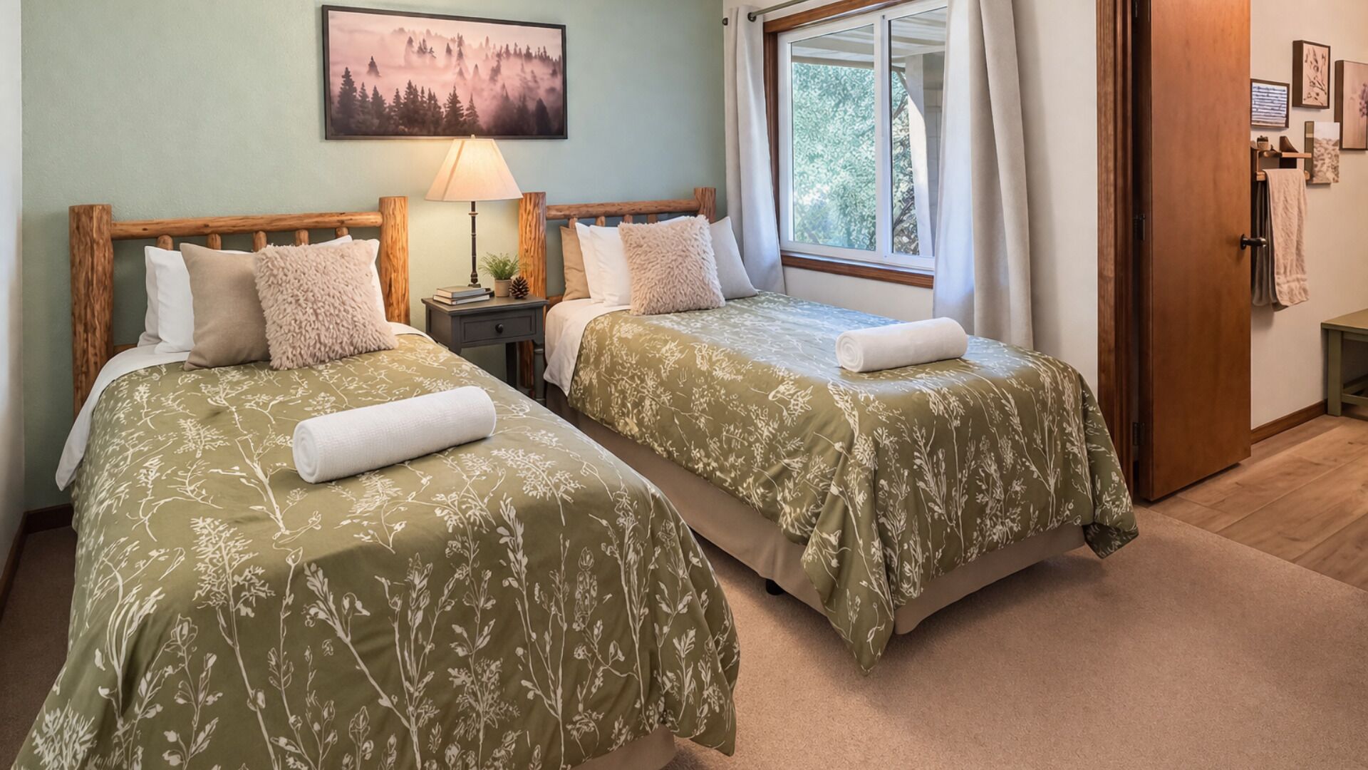 A room with two beds, a nightstand, a lamp, a window with curtains, and a painting on the wall.