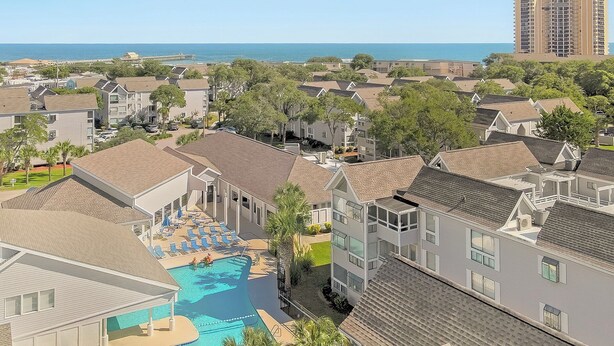 Zona residencial amb piscina, envoltat de cases, vista a l'oceà i un edifici alt al fons.