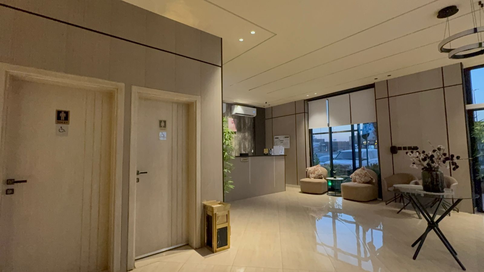 En modern hotellobby med en receptionsdisk, en sittgrupp och stora fönster med utsikt över staden.